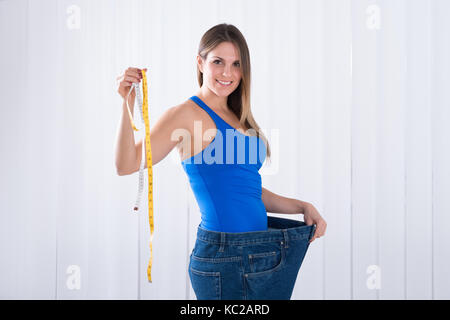 Glückliche junge Frau in Big Jeans Holding Maßband Stockfoto