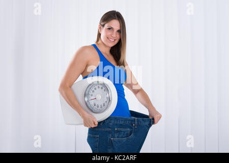 Schlanke junge Frau mit Waagen tragen große Jeans Stockfoto