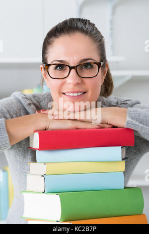 Glückliche Frau lehnte sich auf Stapel von bunten Bücher am Schreibtisch Stockfoto