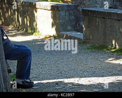 Beine der ältere Mann auf einer Bank mit Sonne und Schatten in Greve in Chianti, Florenz in der Toskana, Italien sitzt Stockfoto