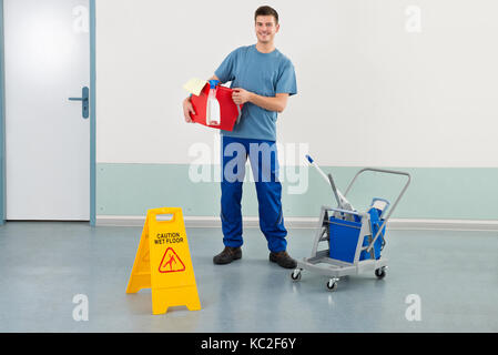 Happy männlichen Arbeitnehmer mit der Reinigung der Geräte und nassen Boden Warnschild Stockfoto