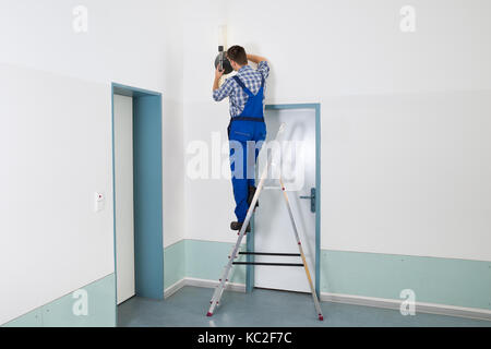 Männliche Elektriker stehen auf trittleiter Instandsetzung Licht Stockfoto