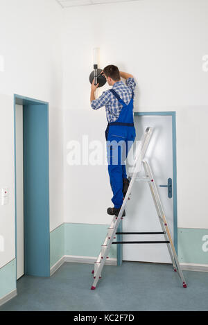 Männliche Elektriker stehen auf trittleiter Instandsetzung Licht Stockfoto