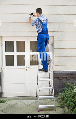 Männliche Techniker auf trittleiter Installation von CCTV-Kamera an der Wand Stockfoto