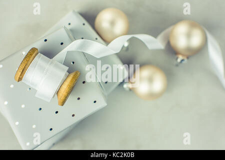 Gestapelte Geschenkboxen in Silber Papier mit Polka Dots Muster gewickelt. Holz- Schieber mit Weiß gewellt Seidenband, Christbaumkugeln auf Stein marmor zurück Stockfoto