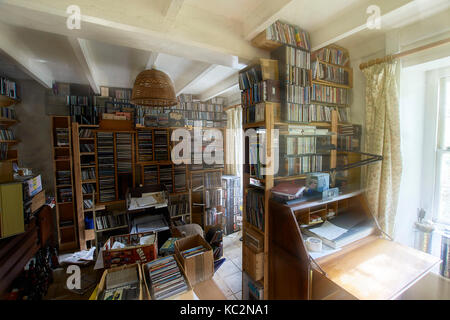 Uriges Haus Innenraum; Zimmer mit Schatten und sonnendurchfluteten Fenstern. Alt fühlen und durcheinandergeworfen Zimmer mit Stühlen, Bücher, CD's und Haus halten. Stockfoto