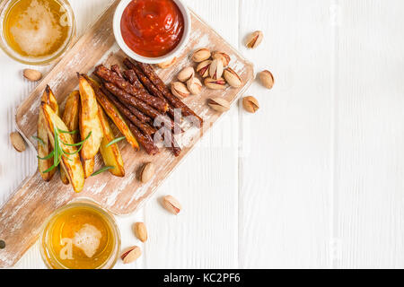 Gläser mit Bier, Kartoffelscheiben und Sauce, Würstchen und Pistazien. Snackbar Menü Stockfoto