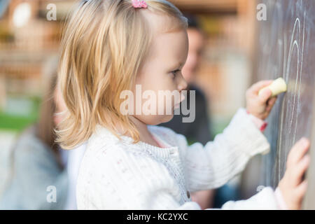 Süße kleine Mädchen Zeichnung auf der Tafel. Kleinkind Mädchen Spaß haben im Freien, Kreide und Zeichnung. Stockfoto