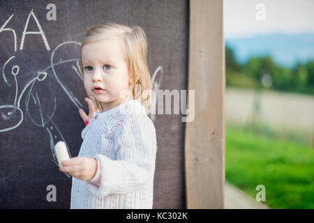 Süße kleine Mädchen Zeichnung auf der Tafel. Kleinkind Mädchen Spaß haben im Freien, Kreide und Zeichnung. Stockfoto