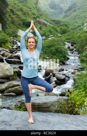 Frau in Yoga Asana Vrikshasana Baum am Wasserfall im Freien Stockfoto
