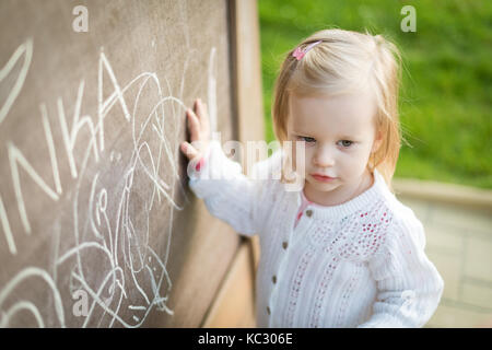 Süße kleine Mädchen Zeichnung auf der Tafel. Kleinkind Mädchen Spaß haben im Freien, Kreide und Zeichnung. Stockfoto