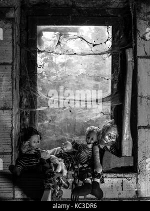 Foto von alten Puppen und eine Axt ruht auf einem alten Fensterbank in Spinnweben und Staub bedeckt. Stockfoto