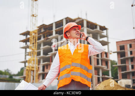 Der junge Architekt trägt einen Schutzhelm auf die Berge Gebäude im Hintergrund Stockfoto