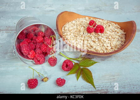 Frische Himbeeren in einen Eimer und Haferflocken in eine hölzerne Schüssel auf eine rustikale Holz- Hintergrund. Gesunde Ernährung, Vegetarische Konzept Stockfoto