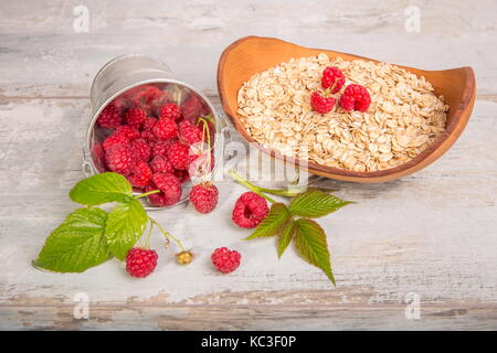 Frische Himbeeren in einen Eimer und Haferflocken in eine hölzerne Schüssel auf eine rustikale Holz- Hintergrund. Gesunde Ernährung, Vegetarische Konzept Stockfoto