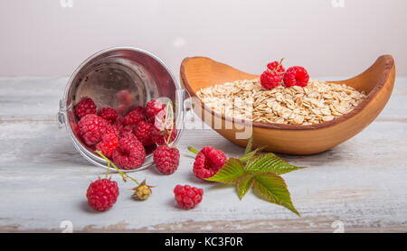 Frische Himbeeren in einen Eimer und Haferflocken in eine hölzerne Schüssel auf eine rustikale Holz- Hintergrund. Gesunde Ernährung, Vegetarische Konzept Stockfoto