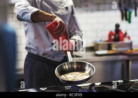 Kaukasische Küchenchef hand gießt Pflanzenöl auf einer Pfanne von der Seite. Stockfoto