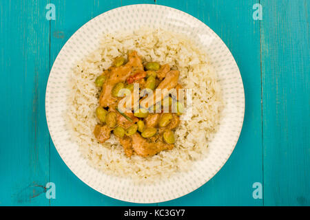 Red Thai Chicken Curry mit Jasmin Reis vor einem blauen Hintergrund aus Holz Stockfoto