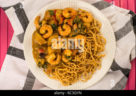 Sri Lanka Style King Prawn Curry mit Nudeln Sitzen auf einem Küchenhandtuch gegen eine Rosa Holz- Hintergrund Stockfoto