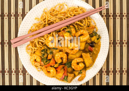 Sri Lanka Style King Prawn Curry mit Nudeln gegen einen hölzernen Bambus Tisch Matte mit Rosa Chop Sticks Stockfoto