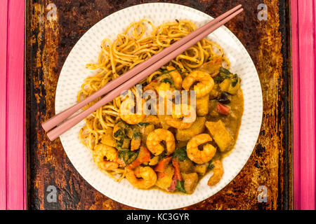 Sri Lanka Style King Prawn Curry mit Nudeln auf einem distressed Backofen oder Backblech mit Rosa Chop Sticks Stockfoto