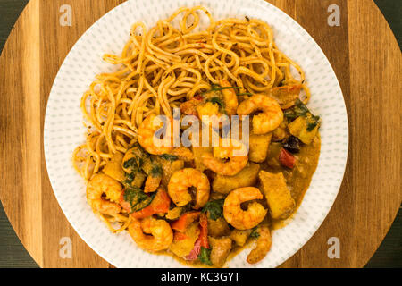 Sri Lanka Style King Prawn Curry mit Nudeln gegen eine Runde Küche aus Holz Schneidebrett Stockfoto