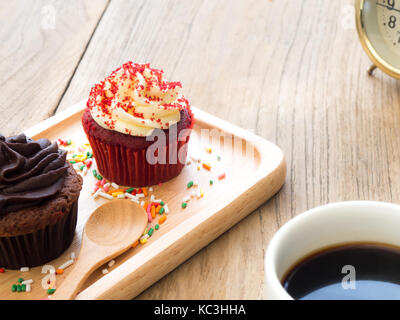 Rot und Chocolate Cupcakes auf einem sphärischen Holzplatte. Neben der Cupcake haben Kakteen und white Coffee Mug. Alle es auf hölzernen Tisch ruht. Stockfoto