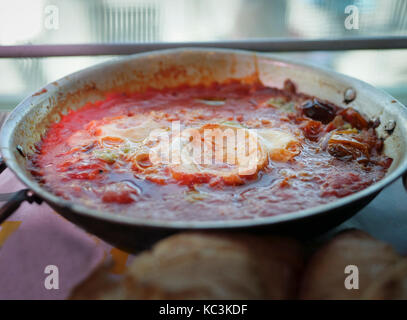Shakshouka oder Shakshuka Gericht der freien Bauernhof Eier mit Tomaten Sauce, Chili, Paprika und Zwiebeln, auf Pan mit frisch gebackenem Brot serviert. Stockfoto
