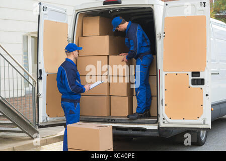 Delivery Man entladen Kartons aus Lkw, während Kollege schreiben auf Zwischenablage Stockfoto