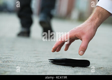 7/8 Hand des Kaufmanns herauf gefallen Brieftasche auf Straße Stockfoto