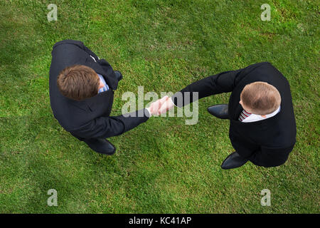 Direkt über dem Schoß der Unternehmer die Hände schütteln beim Stehen auf Wiese Stockfoto