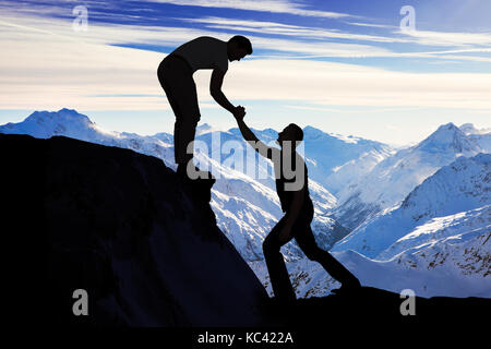 Silhouette junge Mann Unterstützung männlicher Freund in Kletterfelsen Stockfoto