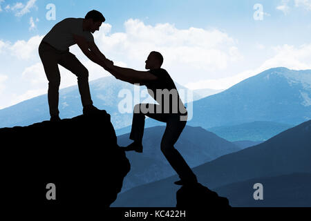 Silhouette junge Mann Unterstützung männlicher Freund in Kletterfelsen Stockfoto