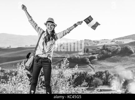 Entdecken Sie magische Ausblicke der Toskana. lächelnden jungen Frau Wanderer in Hut mit Tasche auf der Toskana Wanderung mit italienischer Flagge Stockfoto