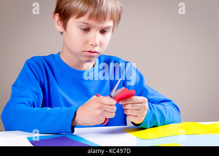 Kind schneiden farbiges Papier mit einer Schere am Tisch Stockfoto