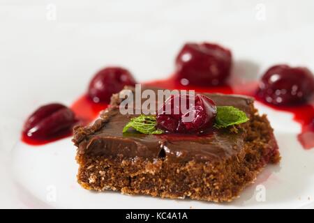 Quadratische Stücke von hausgemachten Brownie serviert auf weiße Platte mit Kirschen und Minze Blätter Stockfoto