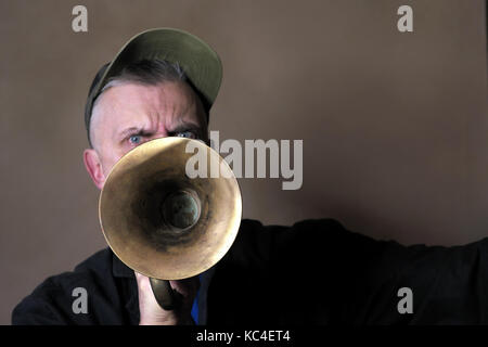Ein Mann mit aggressiven Look spielen alte Hupe, Schwerpunkt in den Vordergrund. Studio Portrait Stockfoto