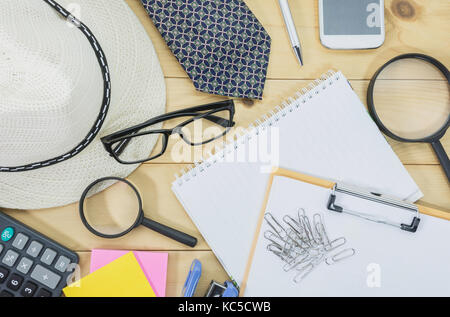 Tabelle Ansicht von oben mit den Gläsern, Notizbuch, Lupe und Handy auf dem Schreibtisch überladen. durcheinandergeworfenen Büro Schreibtisch Hintergrund. Stockfoto