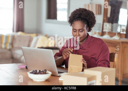 Junge afrikanische Frau Bezettelung von Versandstücken, während die von zu Hause aus arbeiten Stockfoto