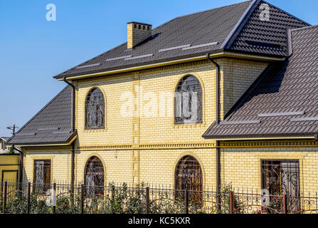 Haus der Yellow Brick und braune Wellpappe Dach aus Metall. Gitter an den Fenstern Stockfoto