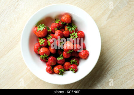 Weißer Keramik Küche Schüssel voll der roten Erdbeeren von einer Antenne Überkopf mit inländischen Zähler Hintergrund genommen. Stockfoto