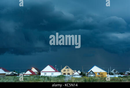 Dunkelblau und Schwarz Regenwolken über Dorf Wohnungen und Häuser wie ein Sturm beginnt Stockfoto
