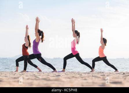 Yoga am Meer Strand am Abend, eine Gruppe von Leuten, die Krieger wirft mit Clam emotion am Strand entspannen, Meditation, Wellness und gesunde Balance Stockfoto