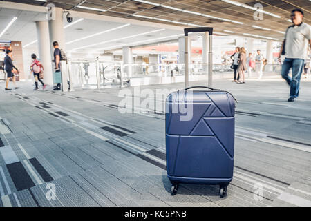 Koffer im Flughafen Abflug Terminal mit reisenden Menschen zu Fuß im Hintergrund, Urlaub, Geschäftsreise, selektiver Fokus auf Koffer Stockfoto