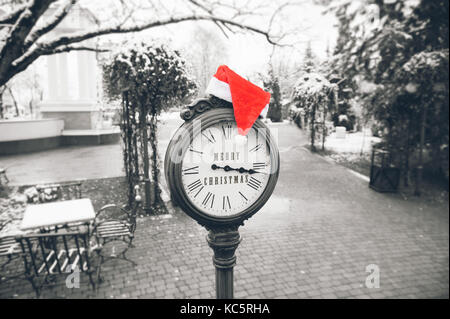 Antike Straße Uhr mit Lügen auf es rote Weihnachtsmütze und der Aufschrift frohe Weihnachten auf Zifferblatt Stockfoto