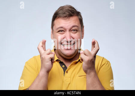 Attraktive fetter Mann im gelben T-Shirt warten auf den besonderen Moment und drückt die Daumen. Stockfoto
