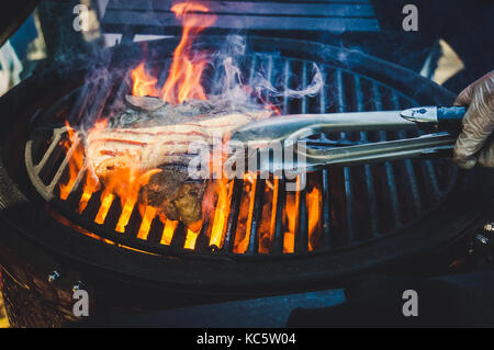 Leckeres Rindfleisch Steaks auf dem Grill mit Feuer flammen. ein Stück Fleisch in der Flamme. . Der Koch spiegelt ein Stück Fleisch Rindfleisch auf dem Grill mit offenen Feuer. Stockfoto