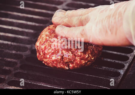 Chef der Hamburger Patty in Küche mit Rinderhackfleisch. hand Koch in einem sauberen weißen sterilen Handschuh, Nahaufnahme berührt die Schnitzel Hamburger gegrillt. Stockfoto