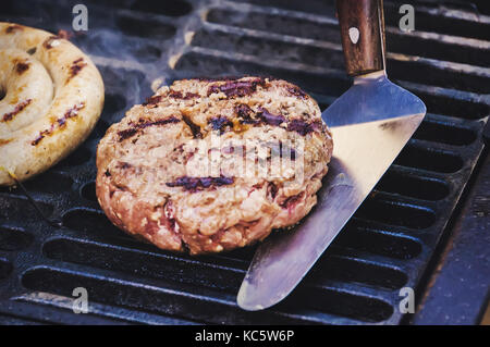 Die Koteletts aus Hackfleisch/Faschiertem gebraten auf den Grill. Fleisch hamburger Patty Nahaufnahme. Zutaten für Burger. Der Chefkoch flips Huhn metall Pfannenwender. Stockfoto