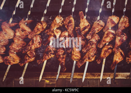 Fried Chicken Beine am Spieß gebraten über Kohle in den großen Grill. Detailansicht von oben. fleischig Chicken Drumsticks mit einem leckeren knusprigen crus Stockfoto